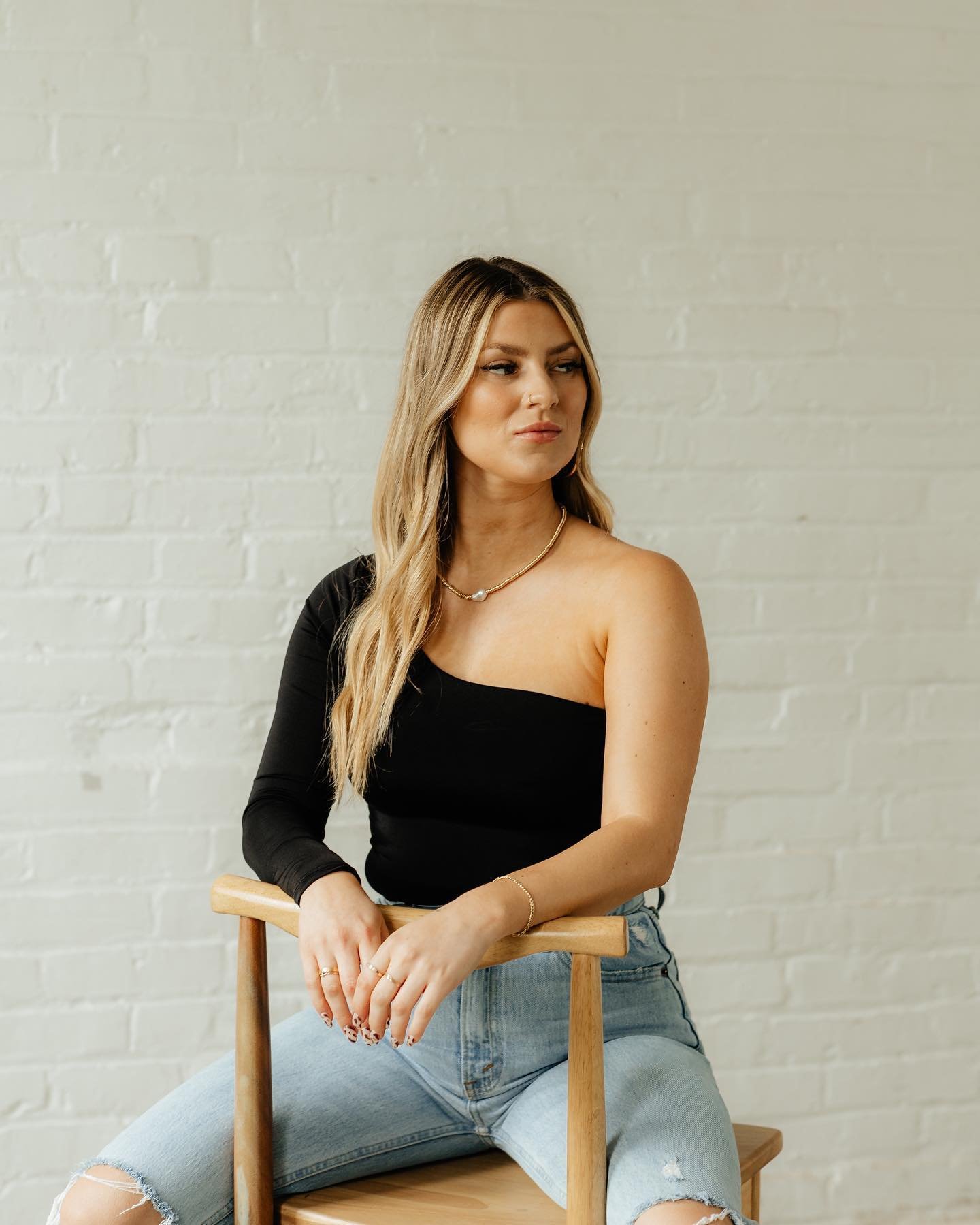 woman sitting on backwards chair and looking to her left by white brick wall