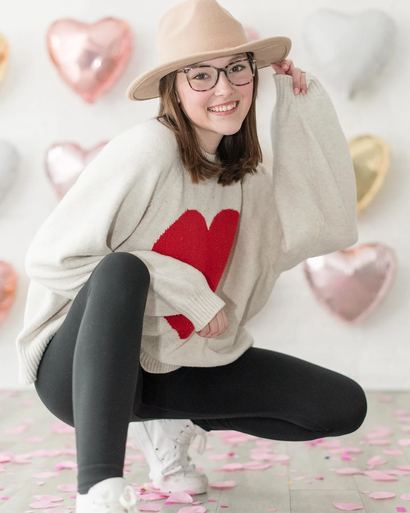 close up photo of girl crouched down and holding edge of her cute hat for valentine's day photoshoot