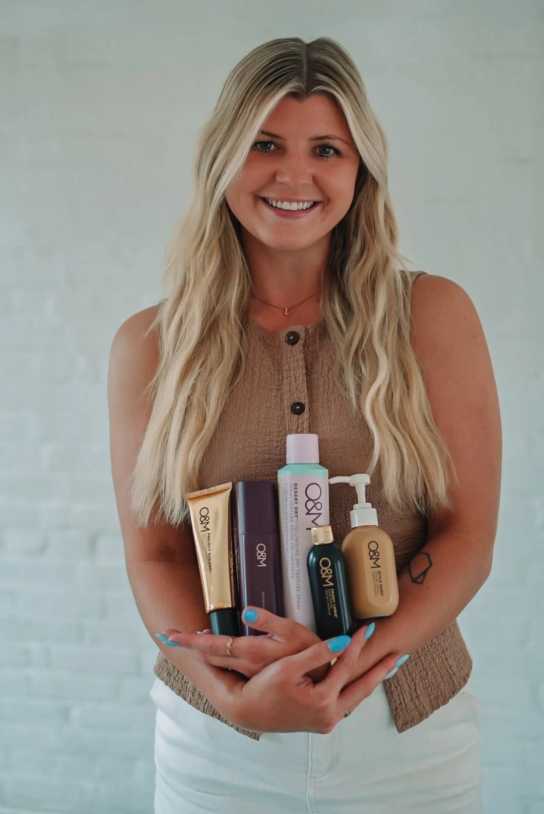 woman holding hair products as she poses for styled brand shoot by white brick wall