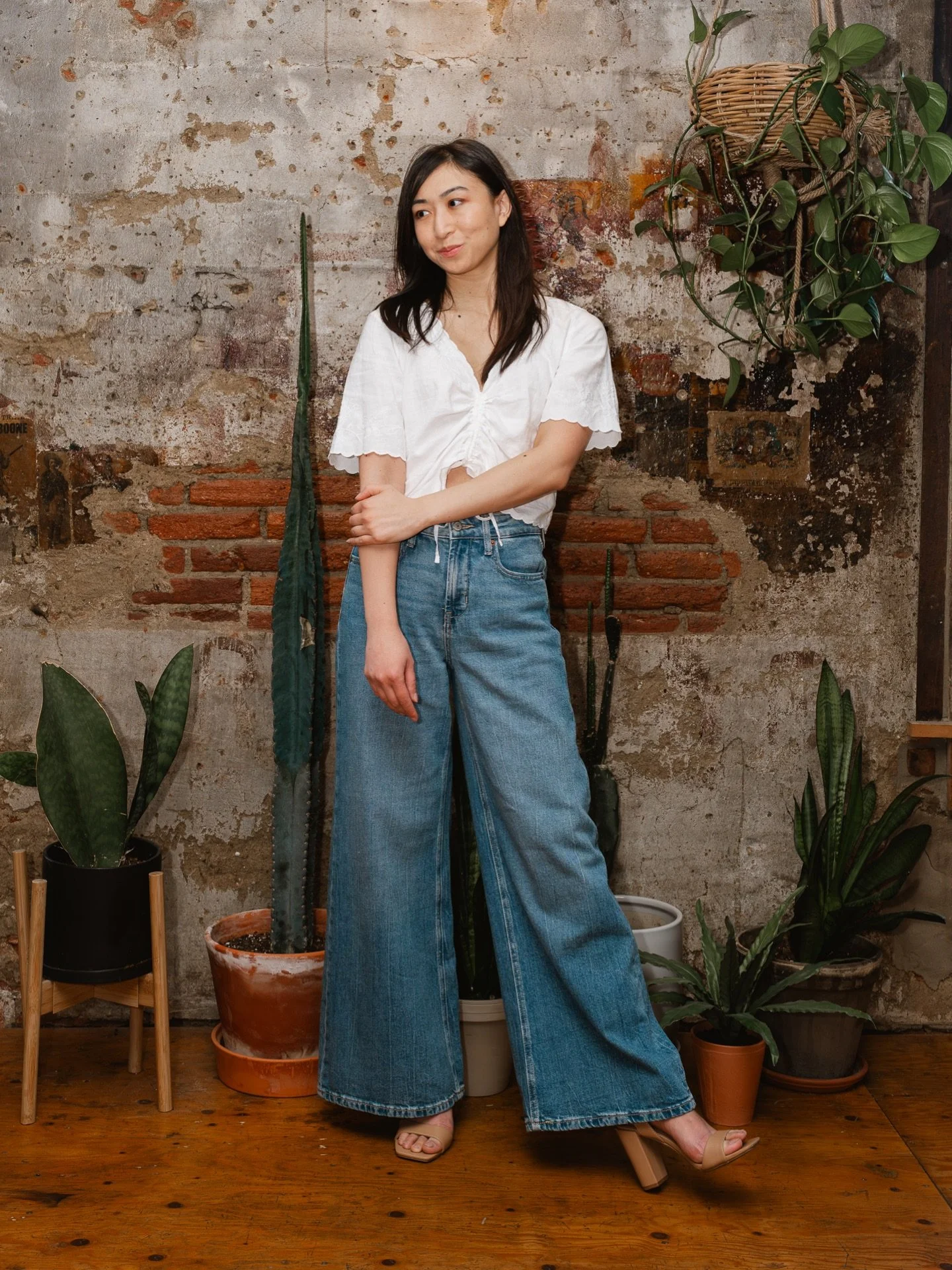 woman standing against exposed brick wall with her left heel out as she looks off into the distance
