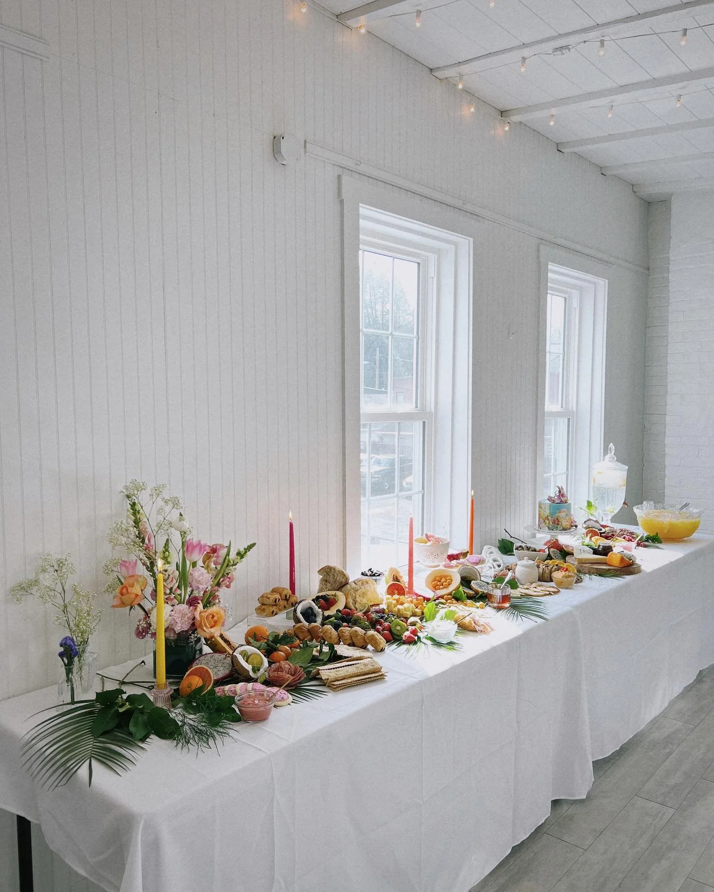two long tables with white linens and beautiful foods and plants displayed all along them