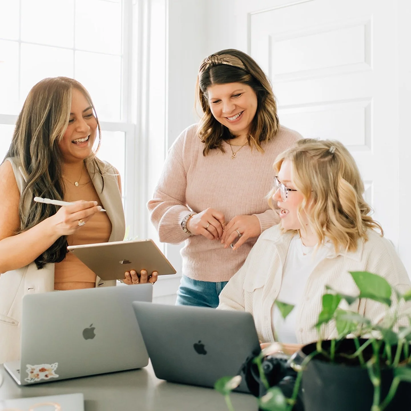 three women standing behind table by their laptops for brand session at The White Room