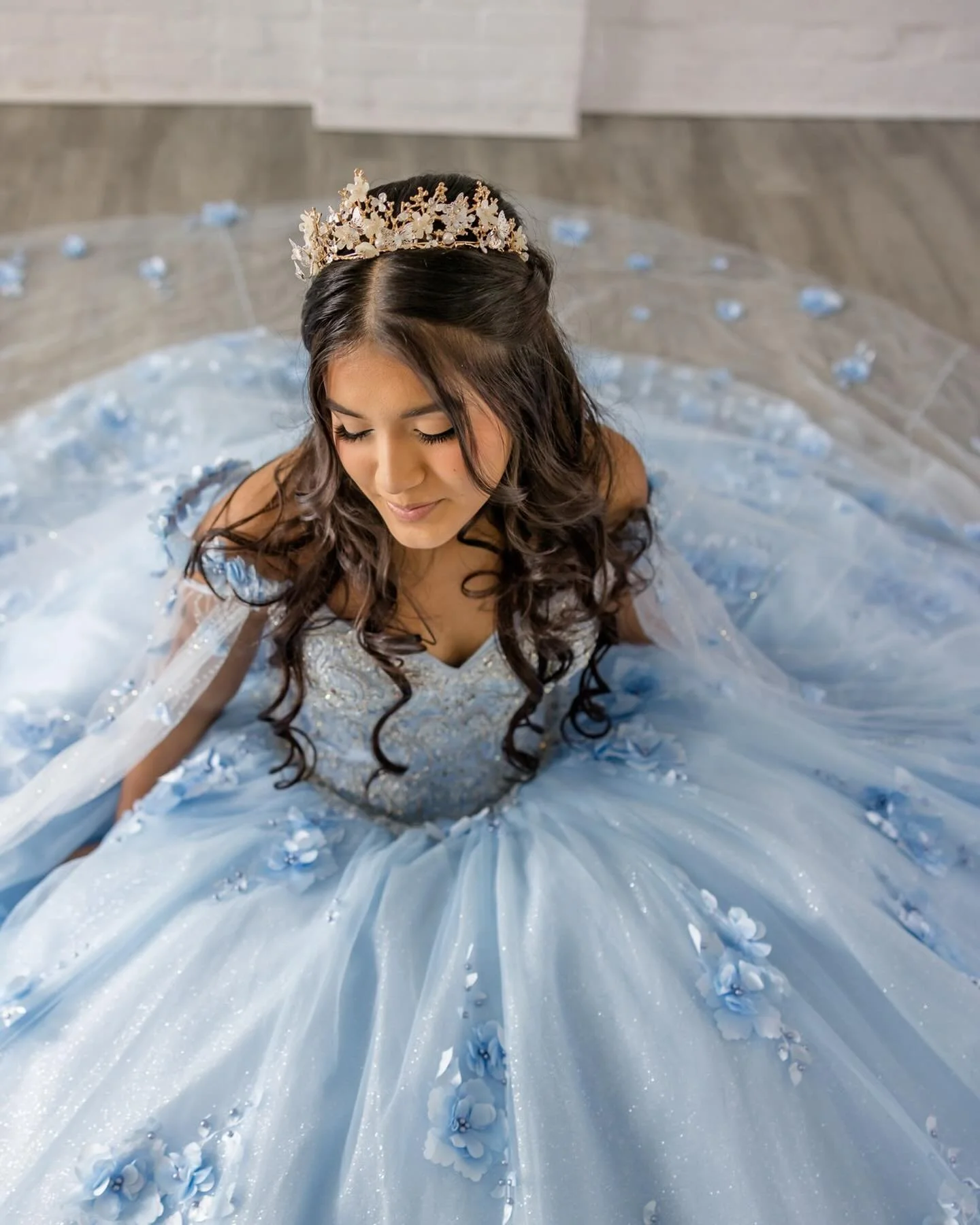 girl sitting on the gray floor wearing stunning light blue gown for her quinceanera 