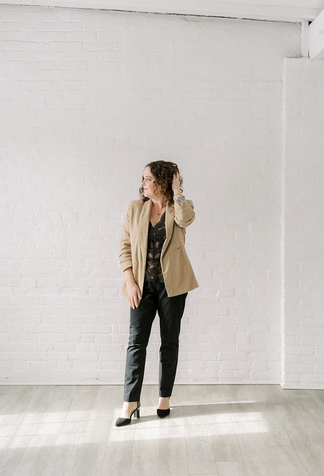 woman posing by white brick wall and looking right with her left hand in her hair at The White Room