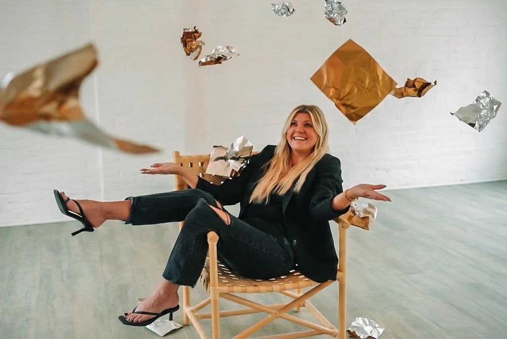woman sitting back in chair and throwing hair foils into the air for styled brand shoot