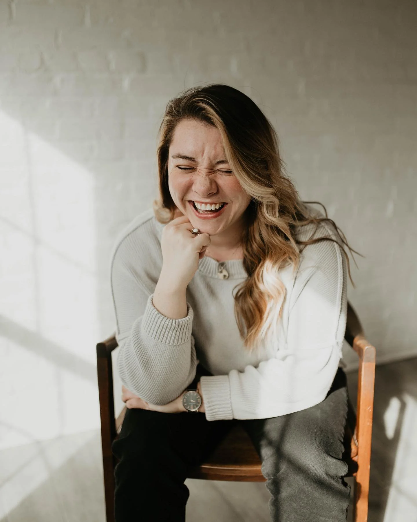 woman sitting on chair and leaning forward on her elbows as she smiles big with her eyes closed
