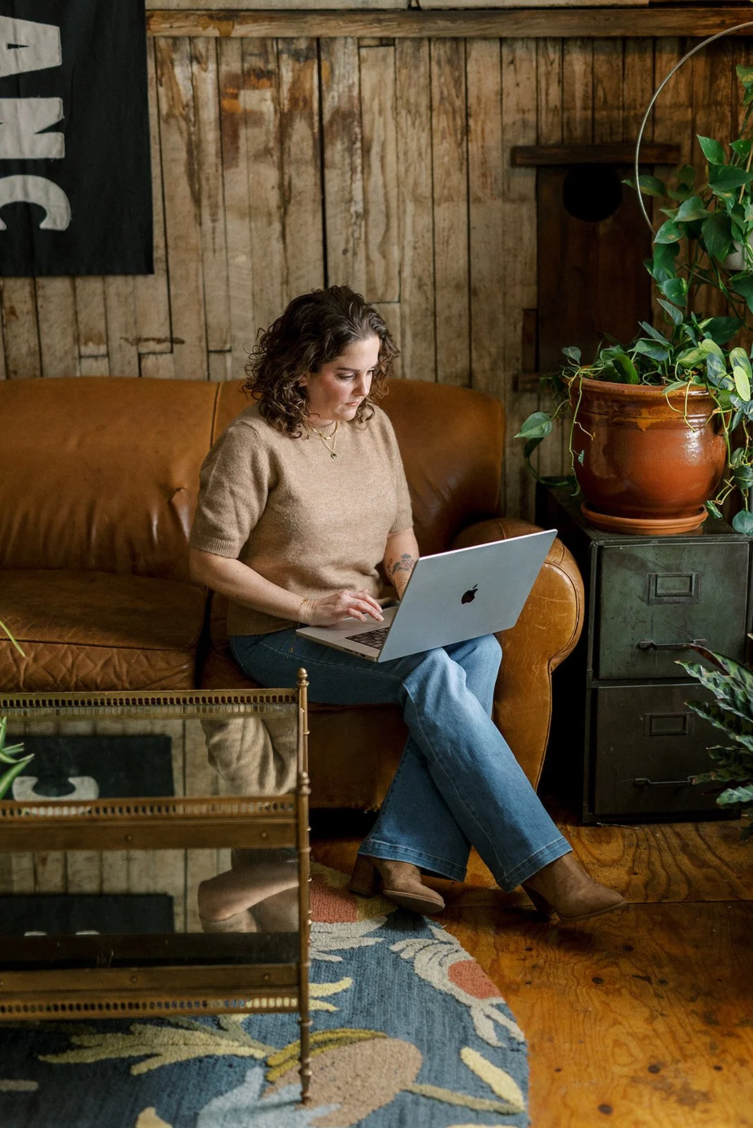woman sitting on leather couch with her laptop in industrial, cozy loft area of The White Room