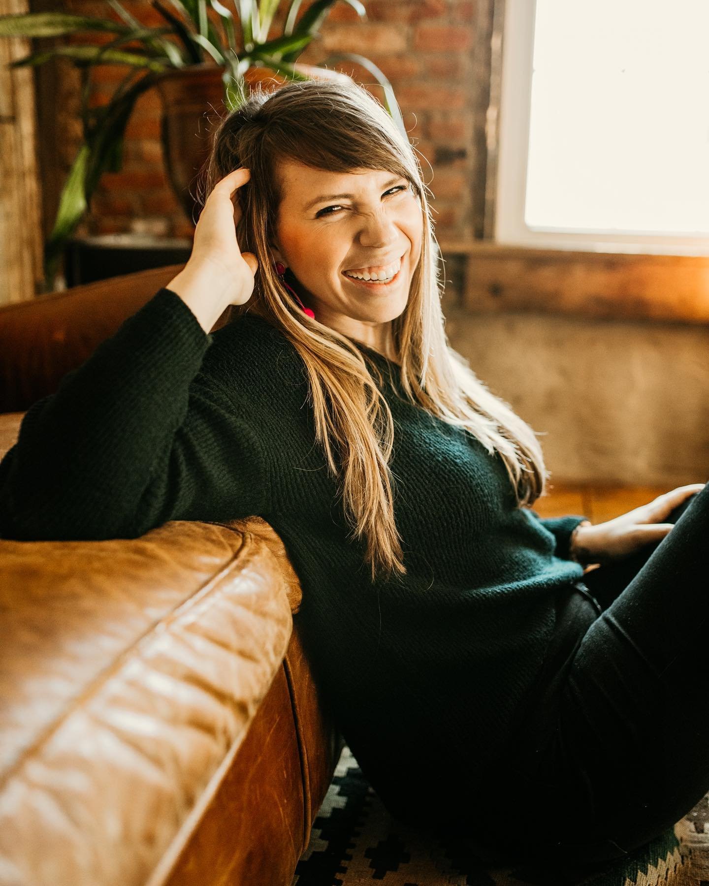 woman sitting on floor and leaning back against leather couch as she rests her right hand on her head and smiles big