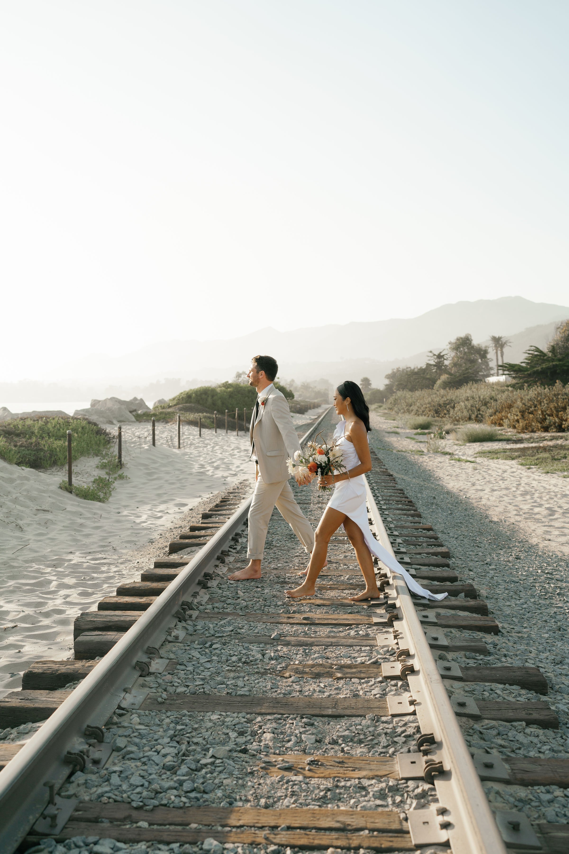 www.santabarbarawedding.com | Rincon Beach Club | Rachel Wakefield | PacWest Blooms | 805 Makeup | Samantha Wagner | Couple Walking Across Train Tracks