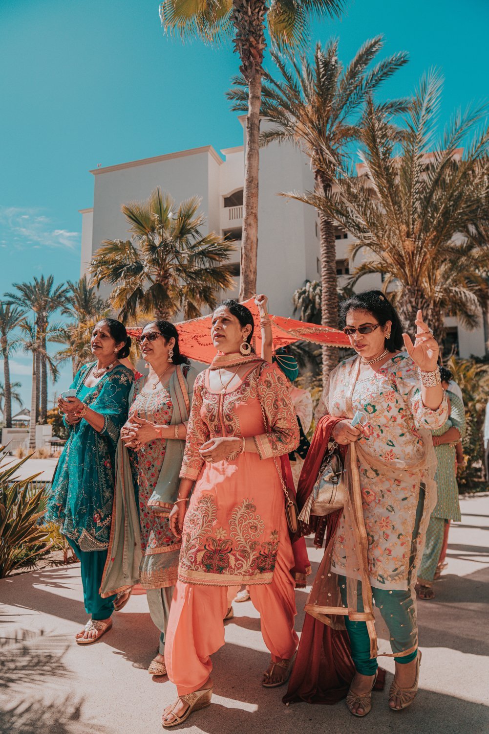www.santabarbarawedding.com | Golden Glow Weddings | Hyatt Ziva Los Cabos | Diego Chavez | Addison Parrish | Female Family Members Walking Groom Under a Colorful Tapestry