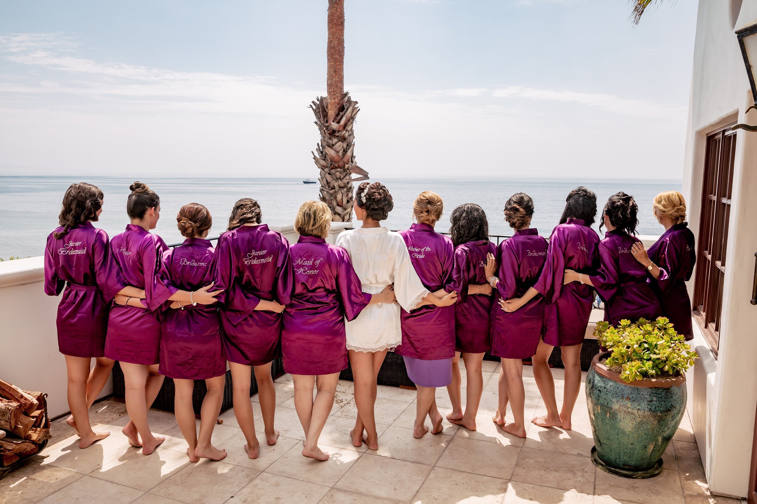 www.santabarbarawedding.com | Rewind Photography | Elegant Sofren Design | Bride and Bridesmaids in Purple Robes Facing Towards the Ocean 