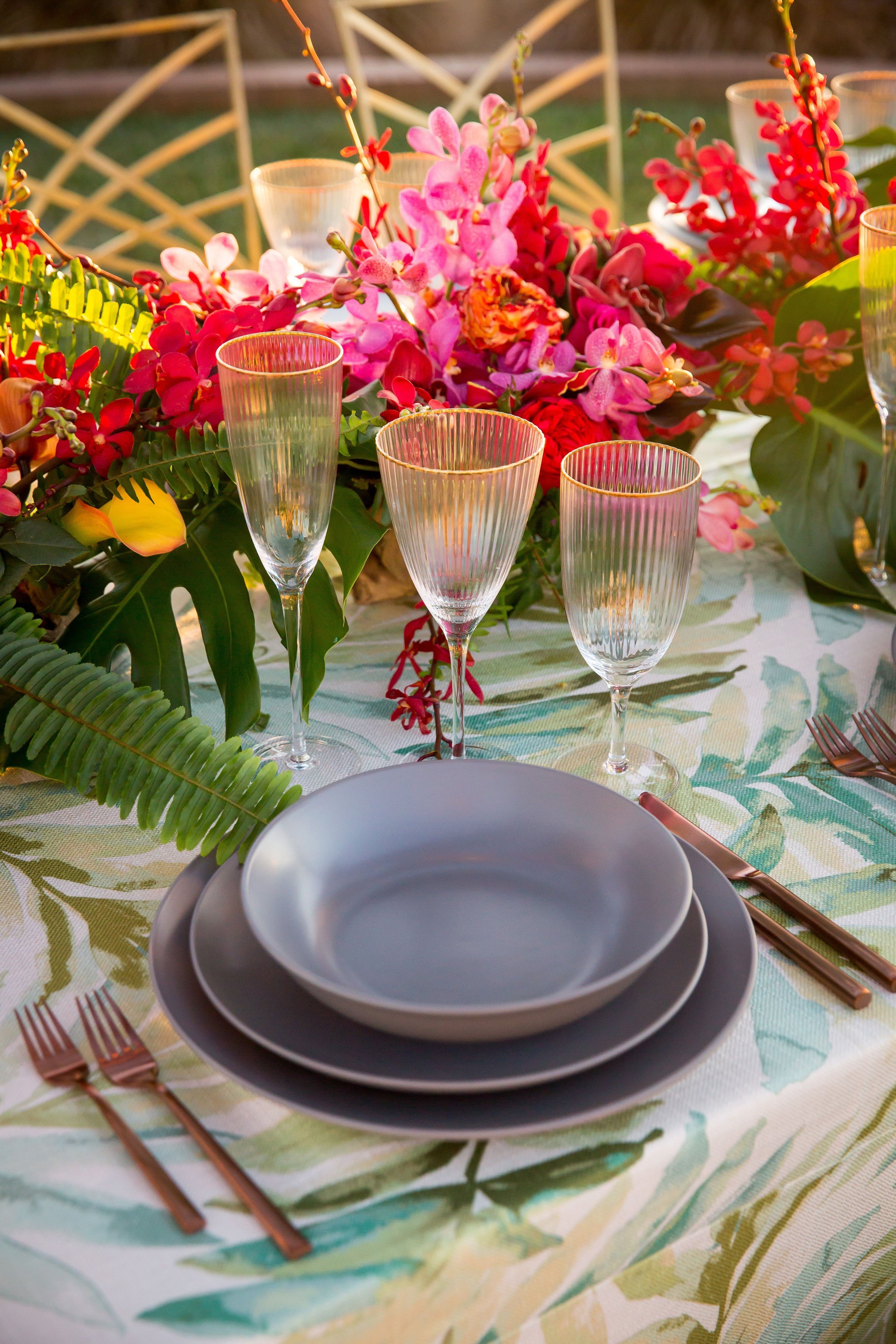www.santabarbarawedding.com | Bright Event Rentals | Vanity Portrait Studio | Place Setting with Grey Plates and a Bowl, Gold Rimmed Glasses, and Colorful Florals All on a Floral Tablecloth