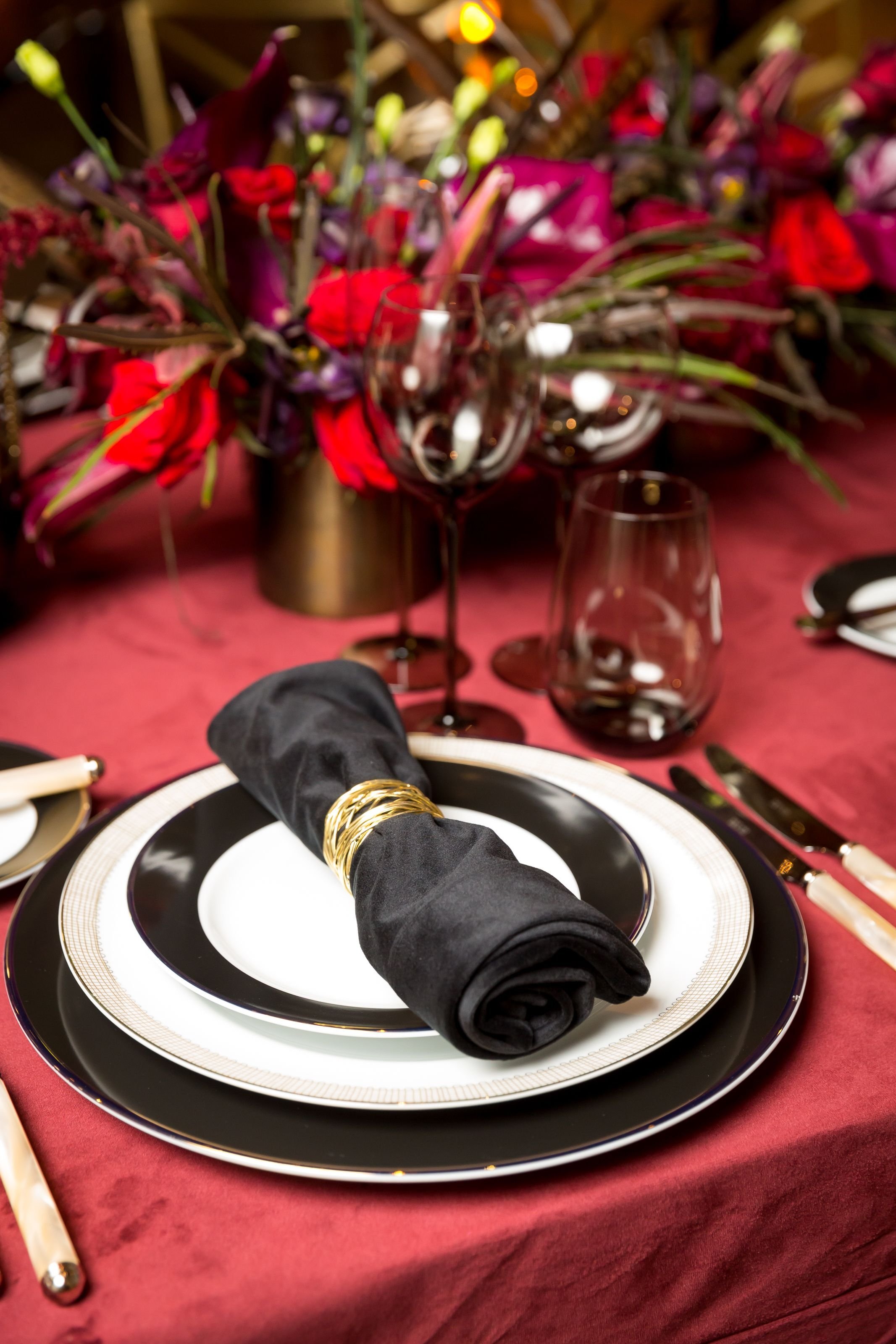 www.santabarbarawedding.com | Bright Event Rentals | Vanity Portrait Studio | Place Setting with Black and White Plates, a Black Napkin, and Glasses on a Red Tablecloth 