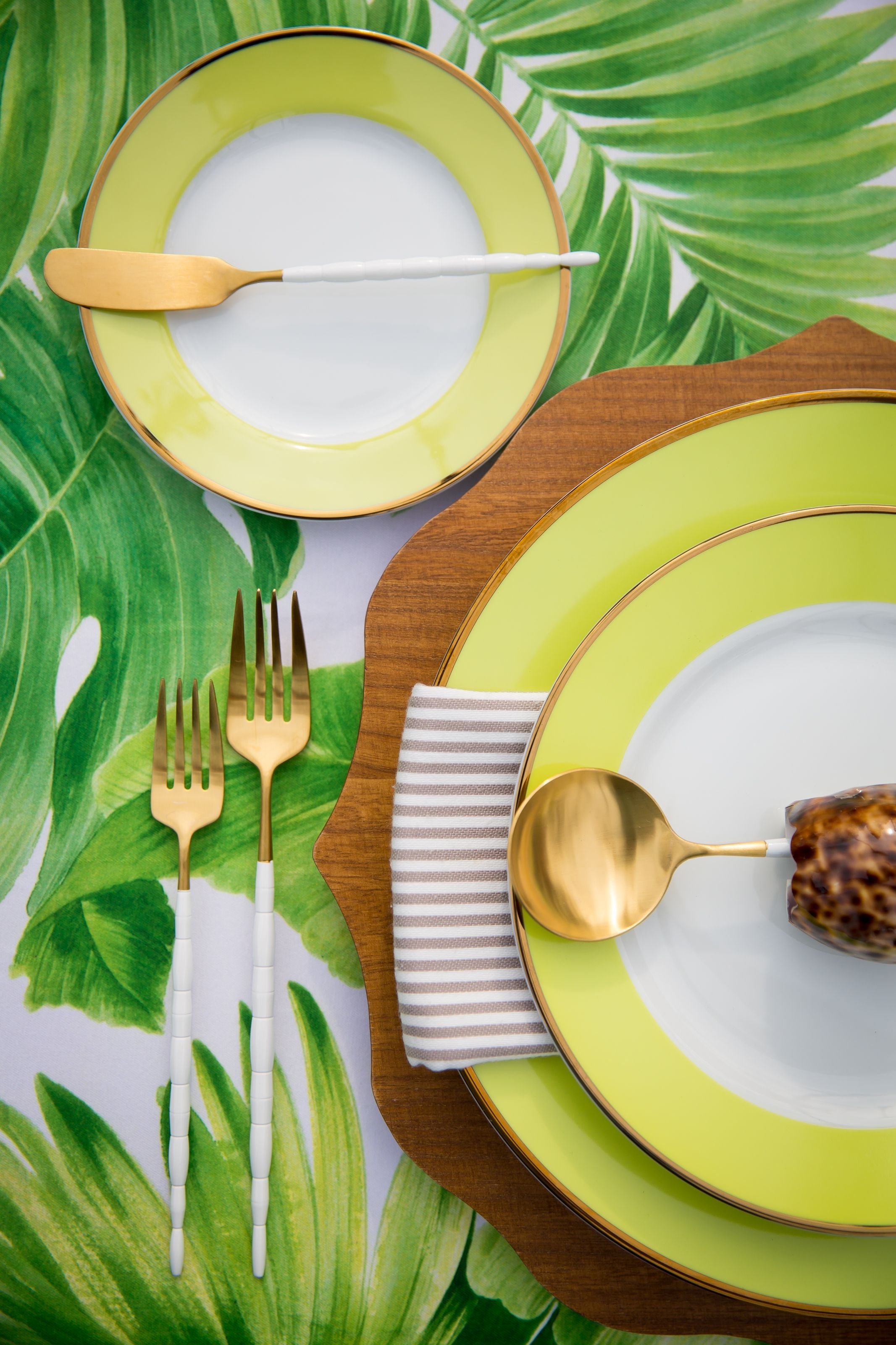 www.santabarbarawedding.com | Bright Event Rentals | Vanity Portrait Studio | Place Setting with Yellow and White Plates and White and Gold Flatware on a Tablecloth of Green Leaves