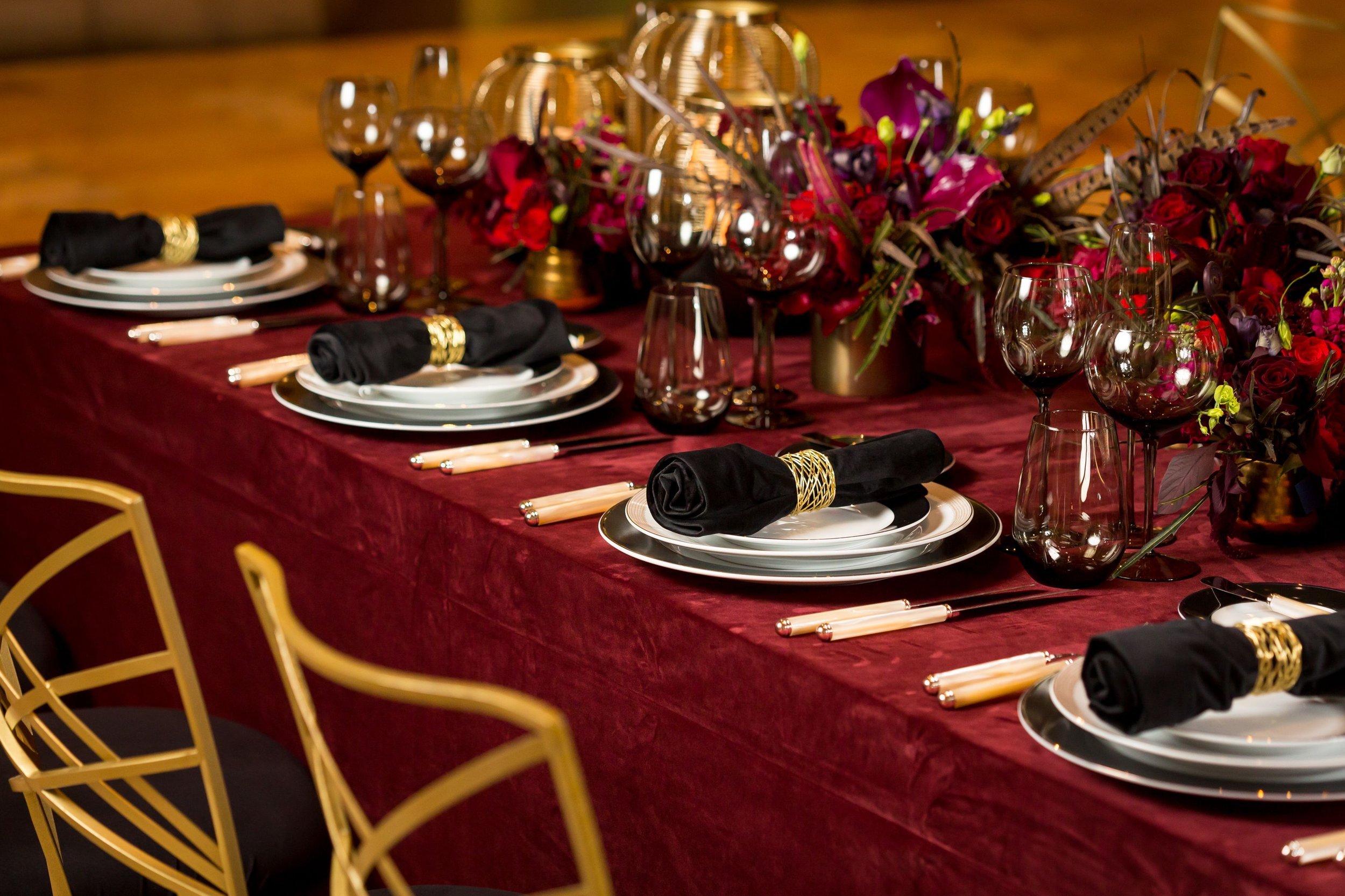 www.santabarbarawedding.com | Bright Event Rentals | Vanity Portrait Studio | Place Settings with Black and White Plates, Black Tinted Stemware, and Silverware on a Red Tablecloth