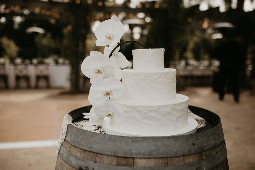 www.santabarbarawedding.com | Lilac Patisserie | White Three-Tiered Wedding Cake with a Textured Design and Large White Flowers on a Wood Barrel