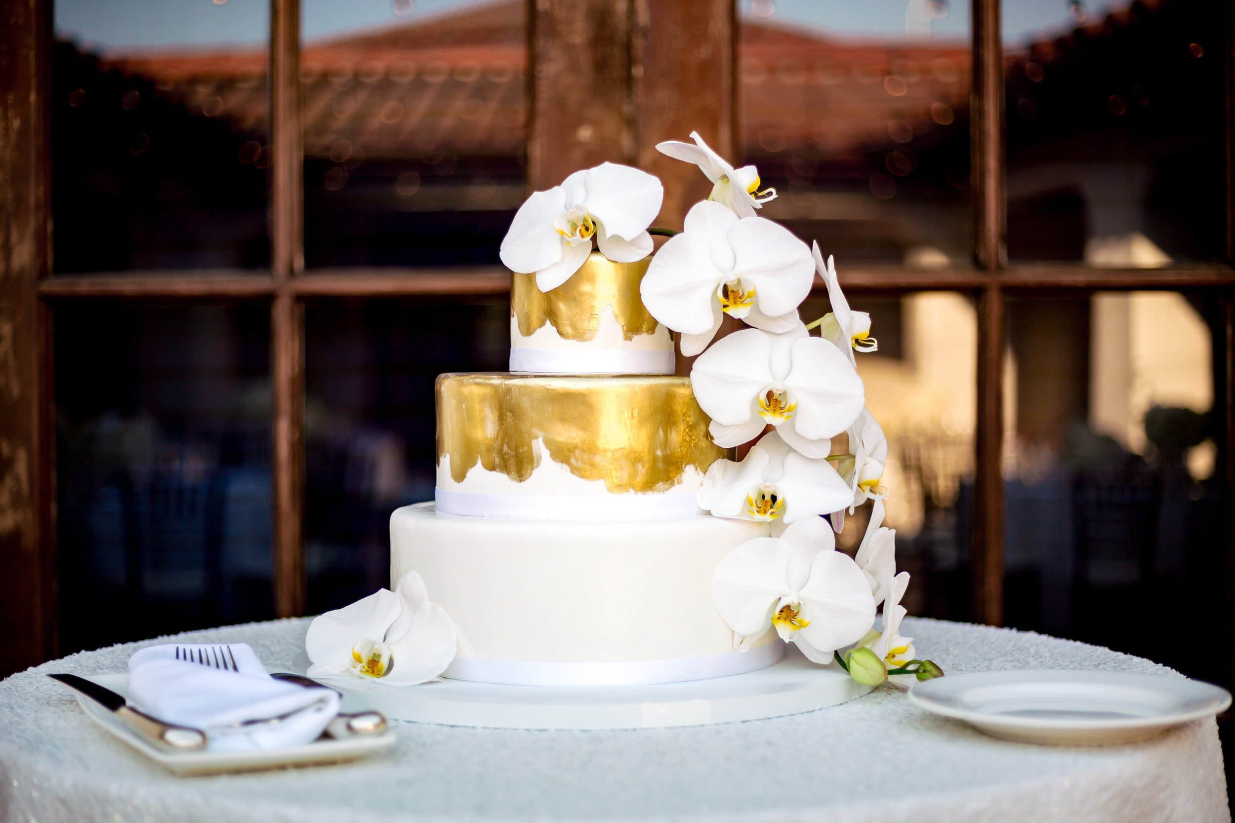 www.santabarbarawedding.com | Lilac Patisserie | Three-Tiered White Wedding Cake with Gold Designs and Large White Flowers
