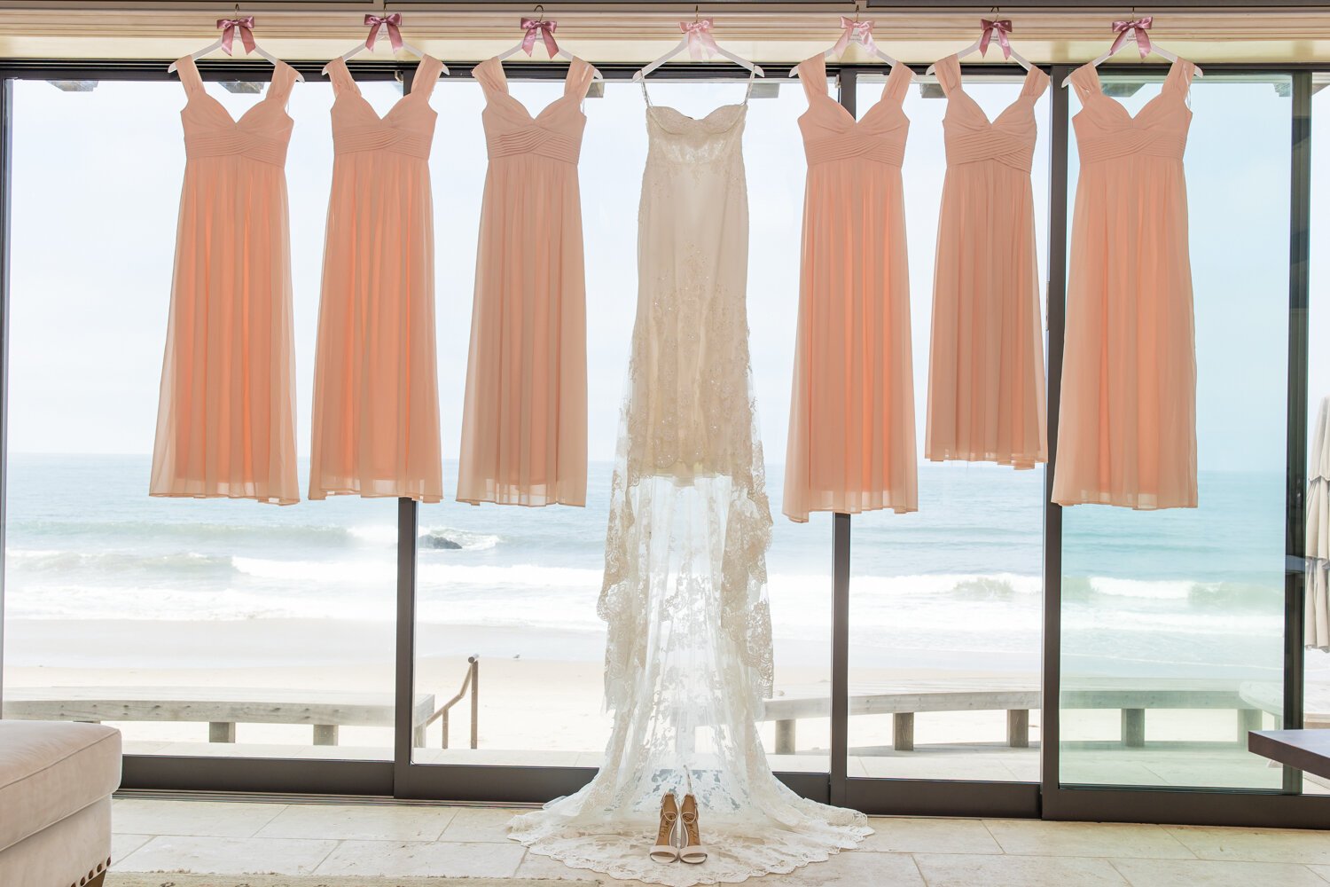 www.santabarbarawedding.com | Elizabeth Victoria | SB Wedding Coordinator | The Bustle | Enzoani | Pacwest Blooms | Wedding Gown and Light Pink Bridesmaid Dresses Hanging with Ocean in Background