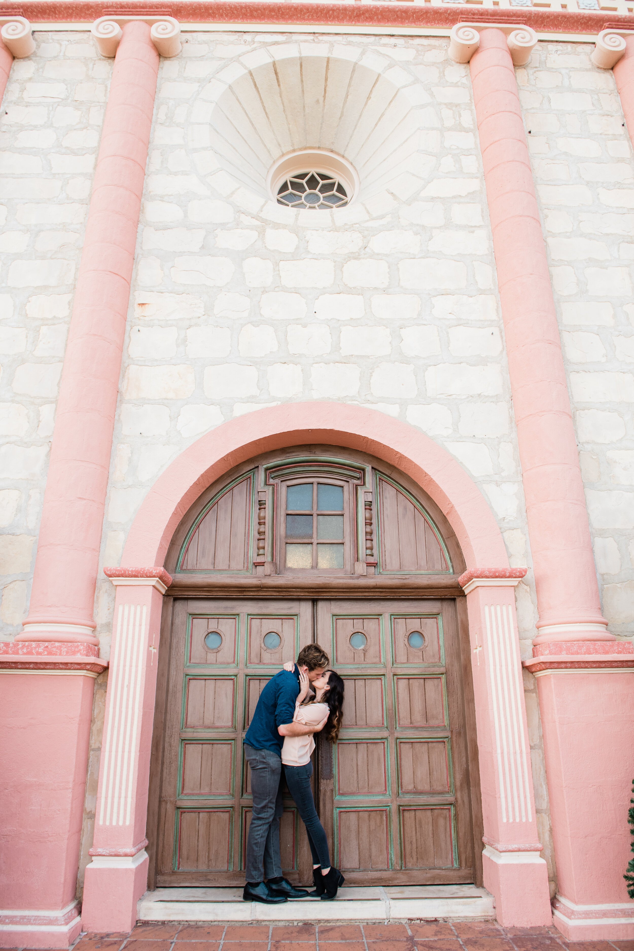 www.santabarbarawedding.com | ByCherry Photography | Old Mission Santa Barbara | Couple Kisses in Front of the Doors of the Pink Old Mission Building 