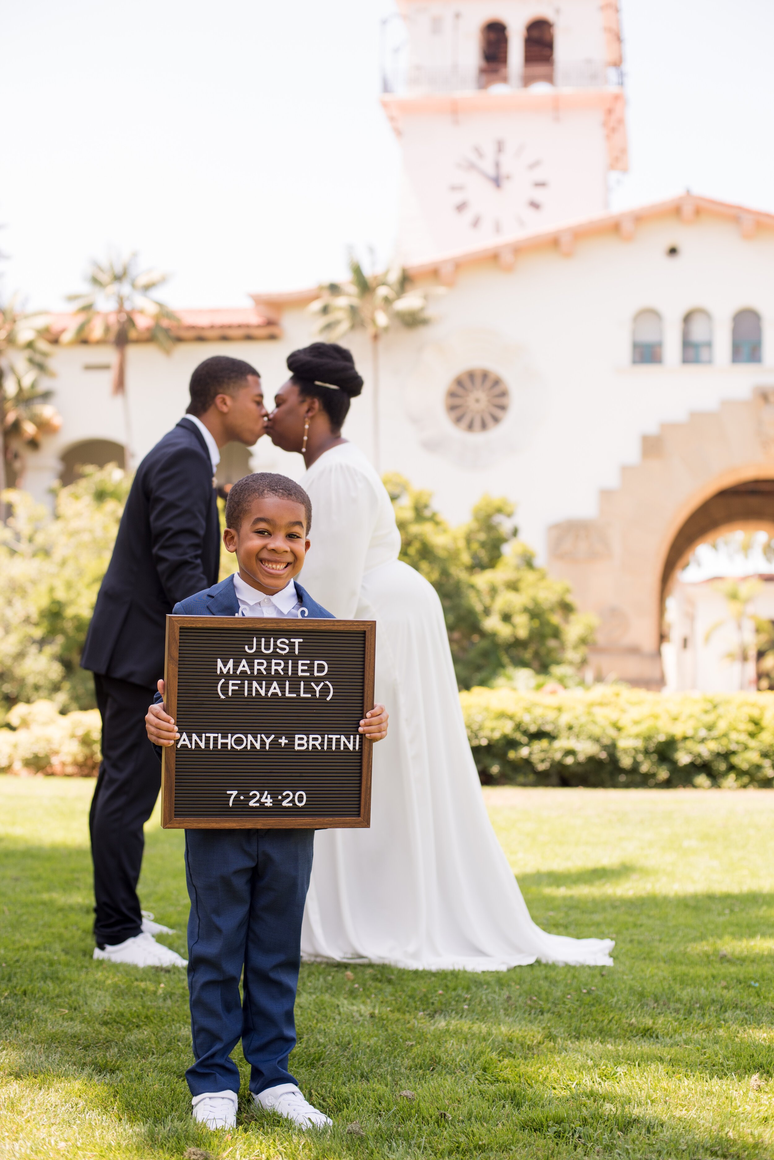 www.santabarbarawedding.com | ByCherry Photography | Santa Barbara Courthouse | Bride and Groom Kiss as Son Holds Up a Just Married Sign