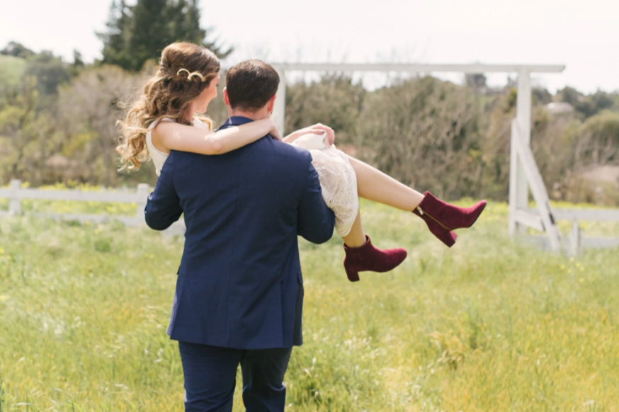 Groom carrying bride through a meadow