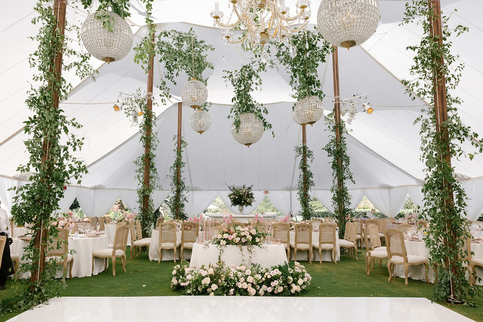 Inside wedding reception tent with round chandeliers and greenery