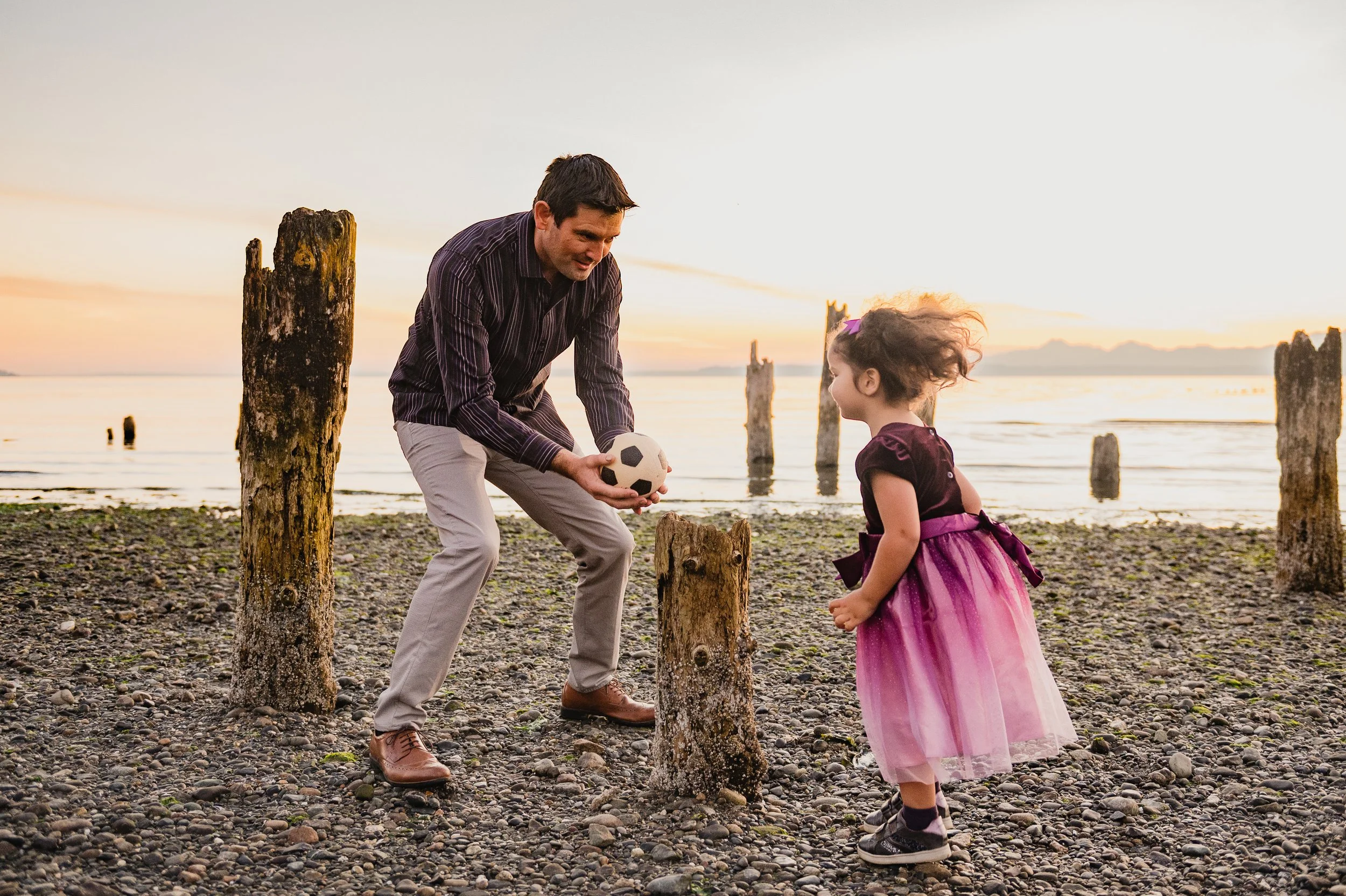 Dad playing soccer with daughter at family portraits in Edmonds on the beach at sunset