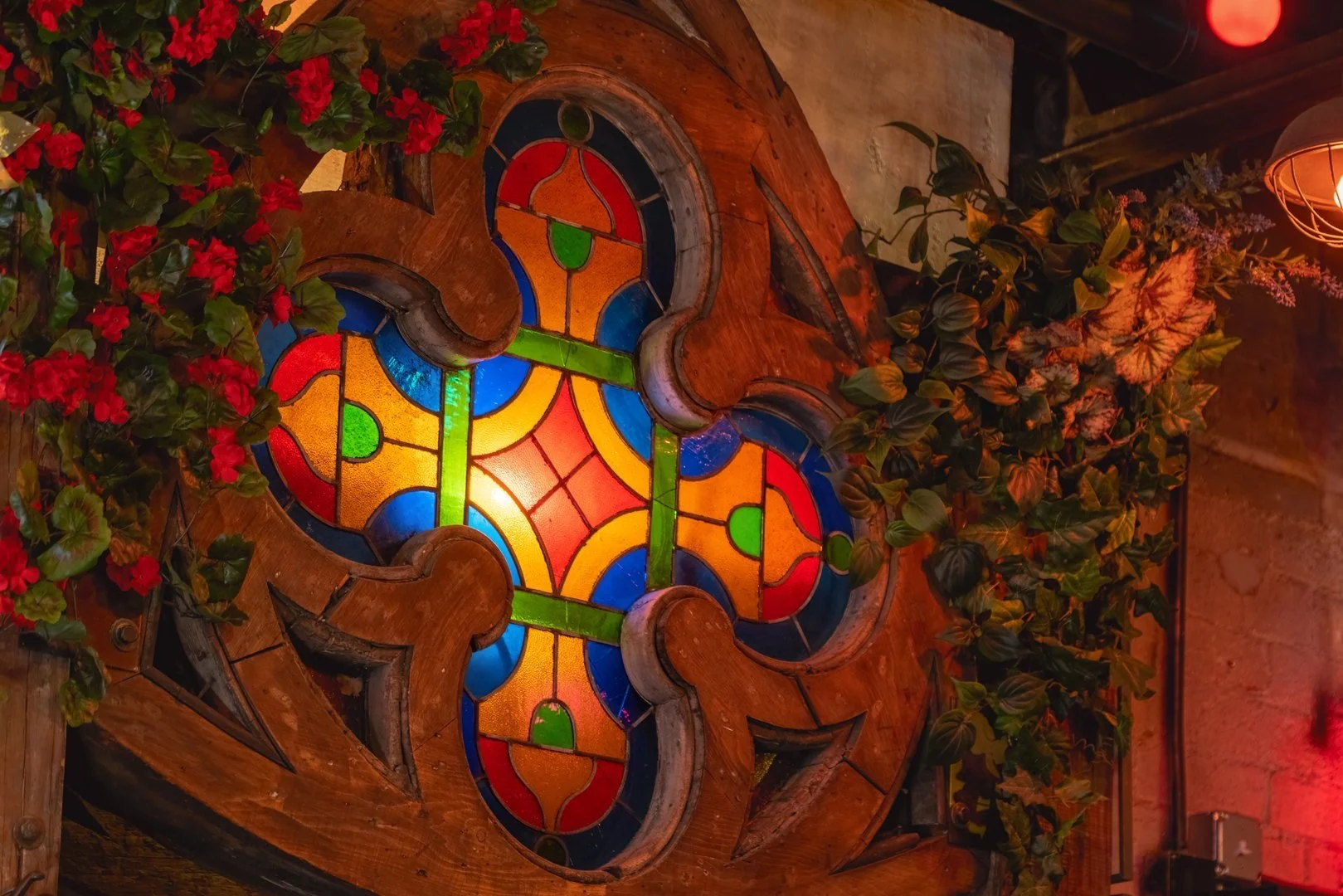Colorful stained glass window with floral design surrounded by red flowers and green leaves