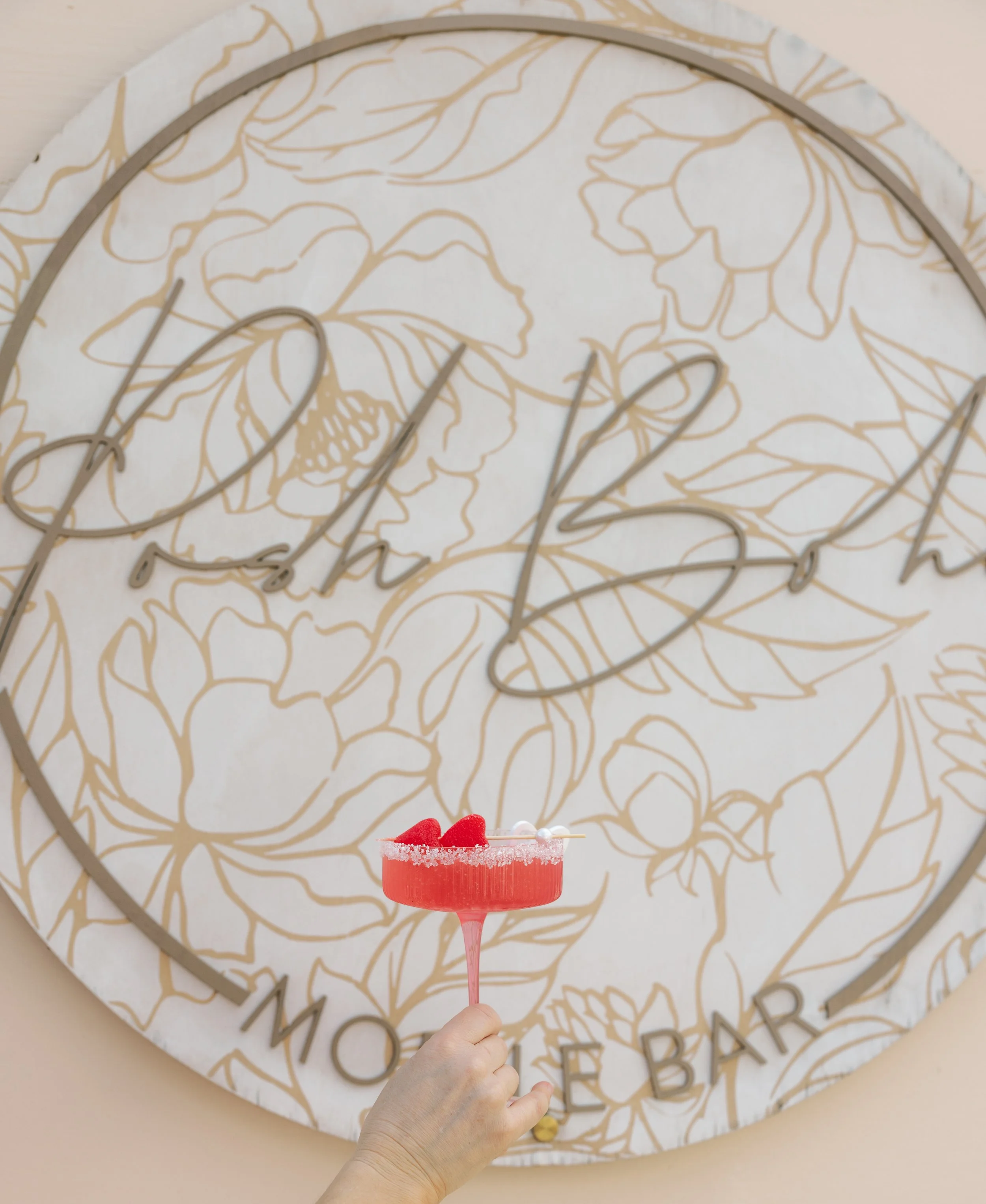 A large decorative clock with floral patterns and the words 'glass house MOORE BAR' on its face, featuring a hand holding a pink drink with a salted rim, strawberries, and a straw in front of it.
