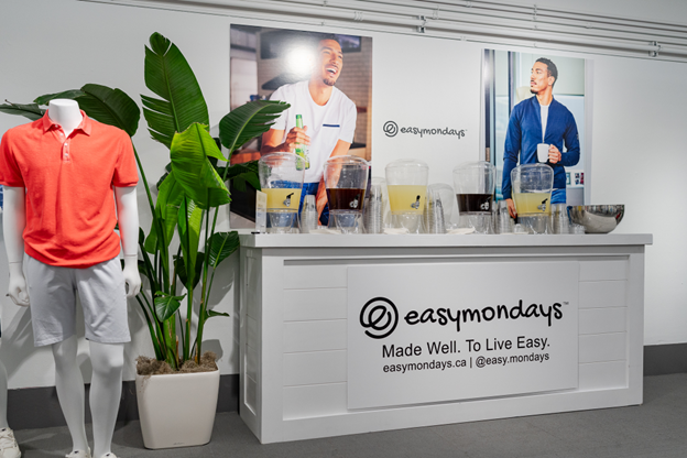 Easymondays reception desk with two large posters of men drinking coffee, potted plants, and a mannequin in casual clothing to the left.