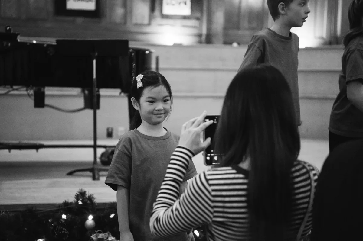 A parent takes a phone photo of a smiling young chorister after a holiday concert