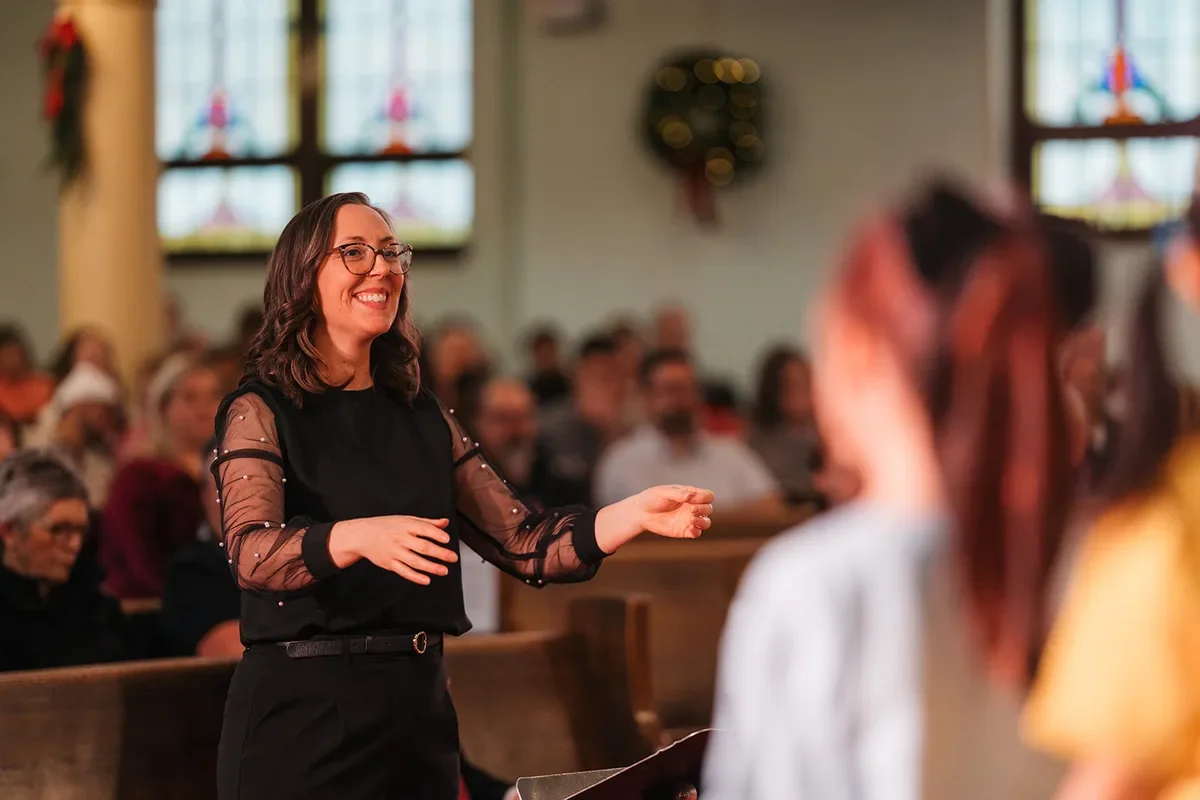 Smiling conductor Sarah Schaub guides young singers during a children's choir concert in Edmonton
