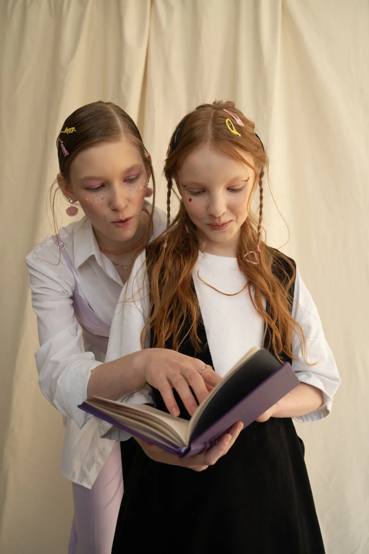Two girls in playful face paint read a storybook together, a quieter choice among after-school activities