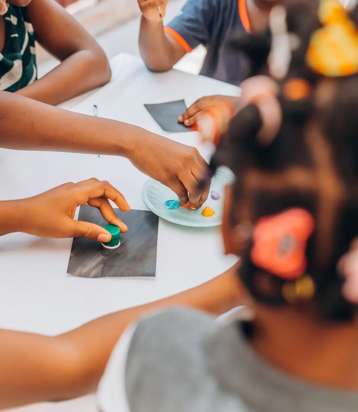 Children stamp paint onto black paper with bottle caps, one of many after-school activities for creative kids
