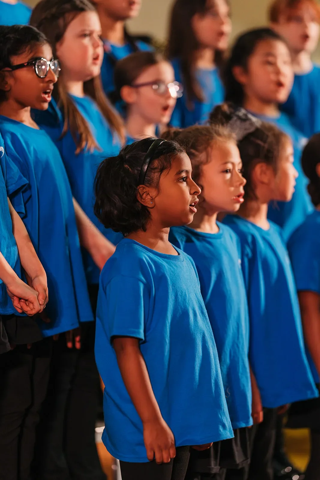 Children in blue T-shirts sing on stage at a holiday concert with their Edmonton after-school choir