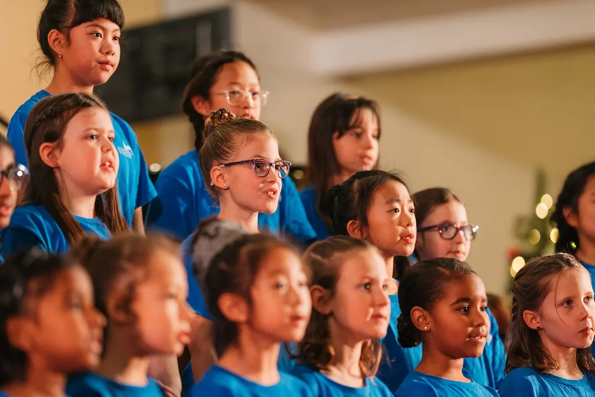Children in blue choir shirts listen and sing together during a holiday concert