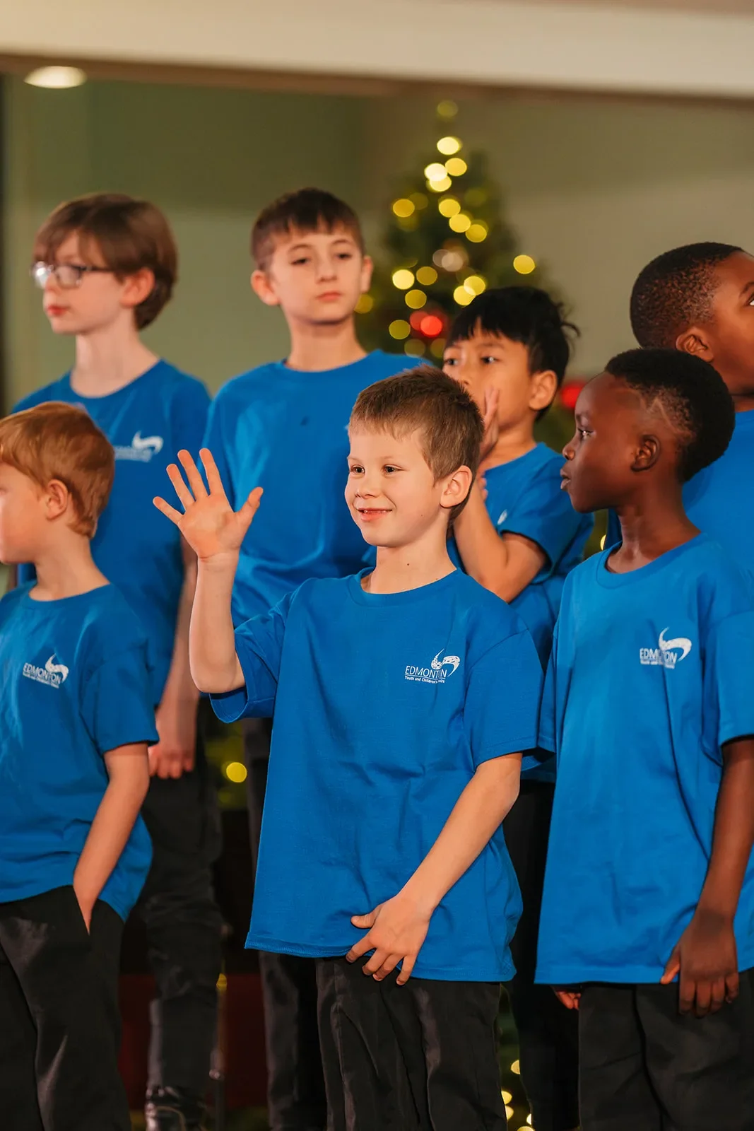 Boys choir members smiling and waving in front of a Christmas tree at a Edmonton holiday concert