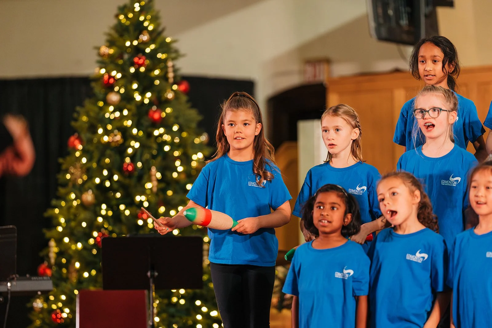 kids choir wearing blue shirts performing next to a christmas tree