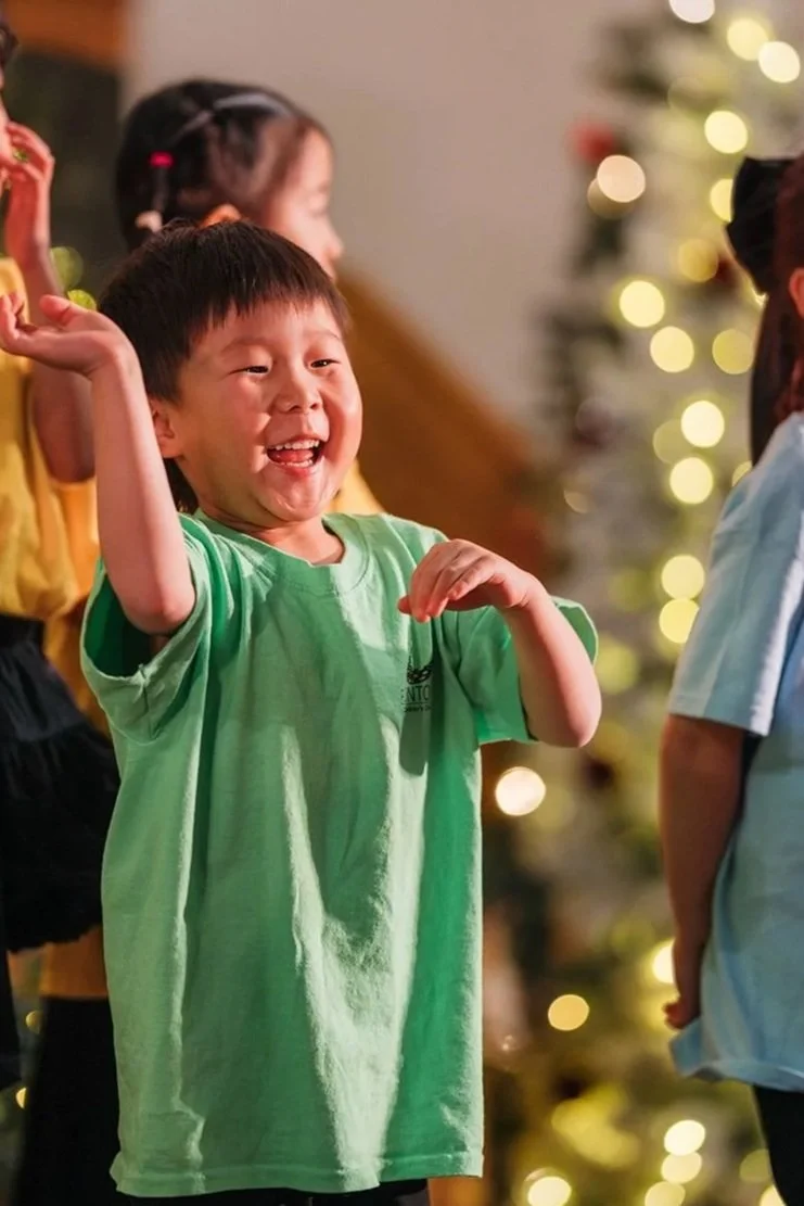one of the angeli singers from edmonton's music classes for kindergarteners waving to his parents during a concert