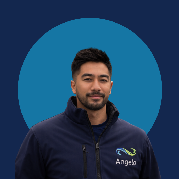 Portret van een man met donkere haar en een baard, gekleed in een donkerblauwe jas met een logo en de naam 'Angelo' erop, staand voor een achtergrond met een grote blauwe cirkel.