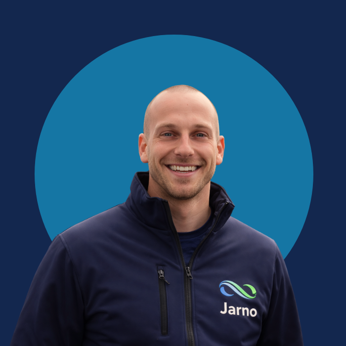 Man in een donkerblauwe jas met een glimlach, logo 'Jarn' zichtbaar.