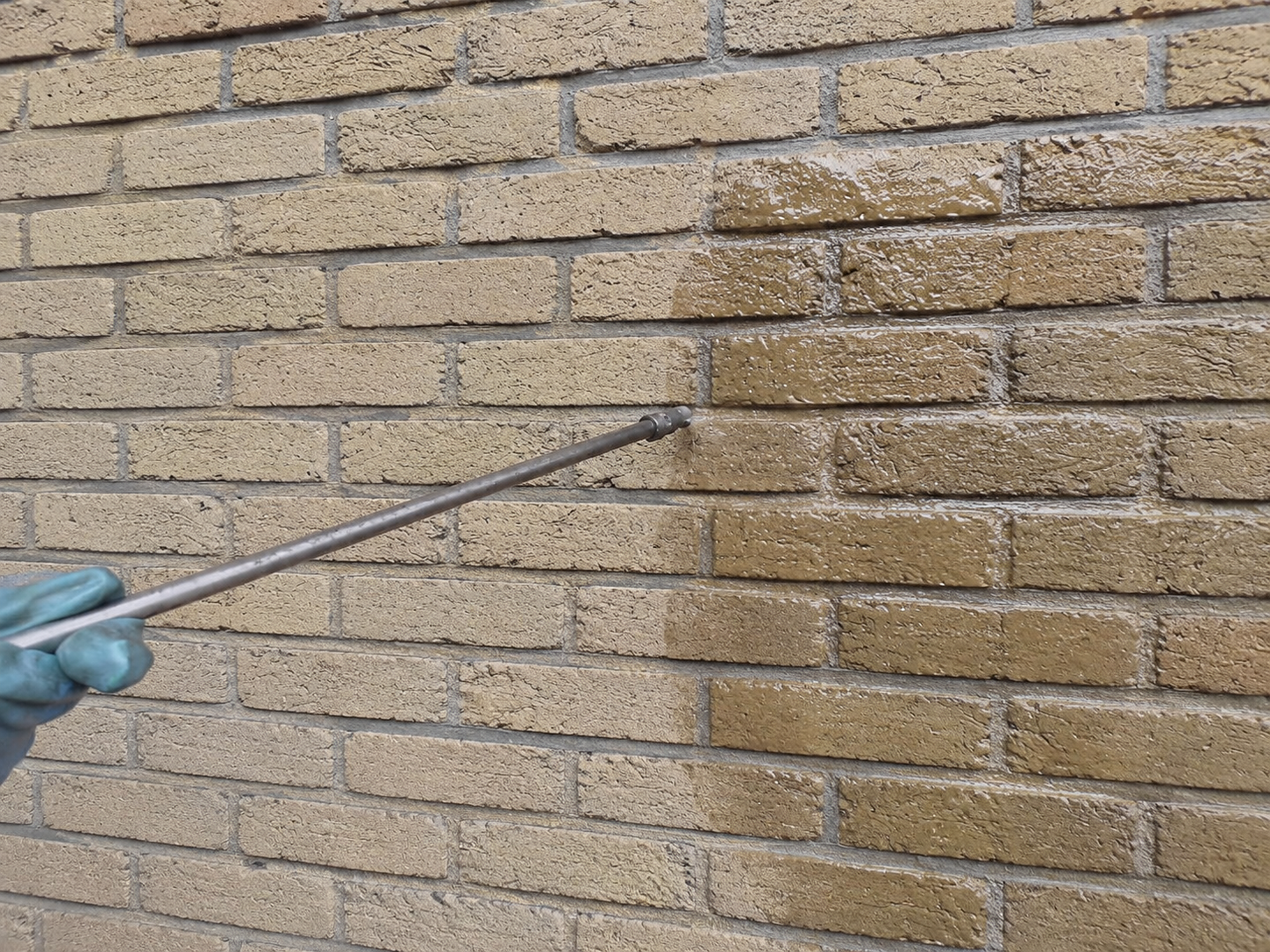 Persoon die een hogedrukreiniger gebruikt om een bakstenen muur schoon te maken.