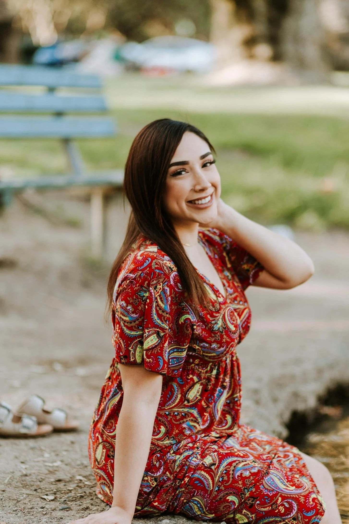Smiling woman in a red paisley dress sitting outdoors near a bench