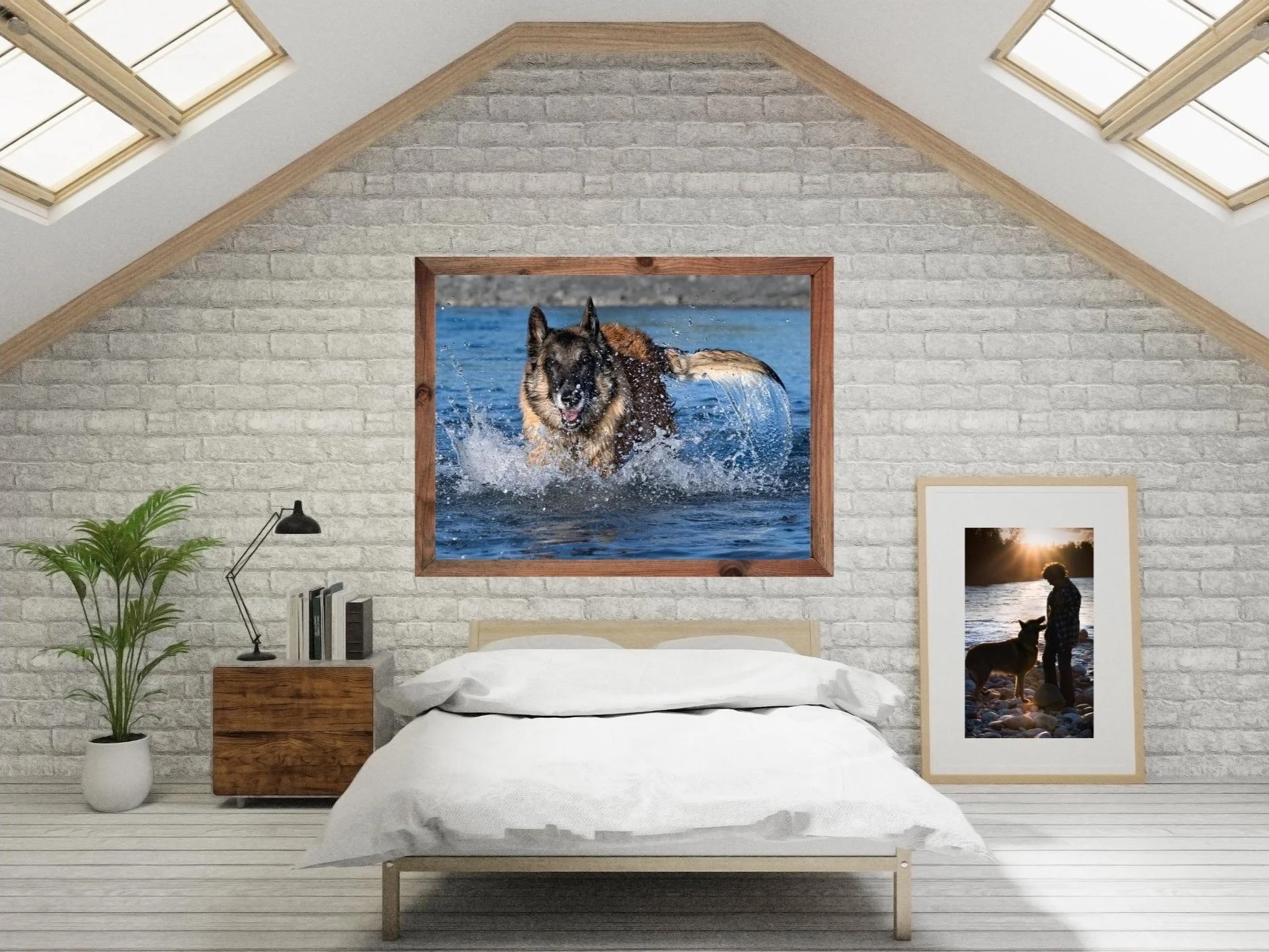 Interior of a bedroom with a white bed, a brick wall, and wall art including a large framed photo of a dog running in water. There is a potted plant on the left, a black desk lamp on a side table, and themed pictures on the wall, including a sunset scene with a person and a dog.