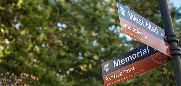 Two street signs at UBC representing English names (West Mall and Memorial) as well as names in hən̓q̓əmin̓əm̓ (sm:entásəm, 'facing the mountains' and šxʷhək̓ʷmət, 'that which used to remember them').