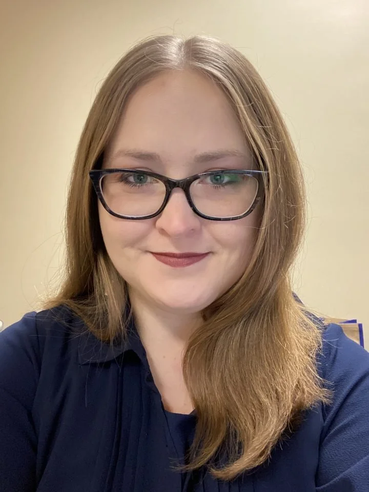 A smiling, blonde haired person infront of a light yellow background