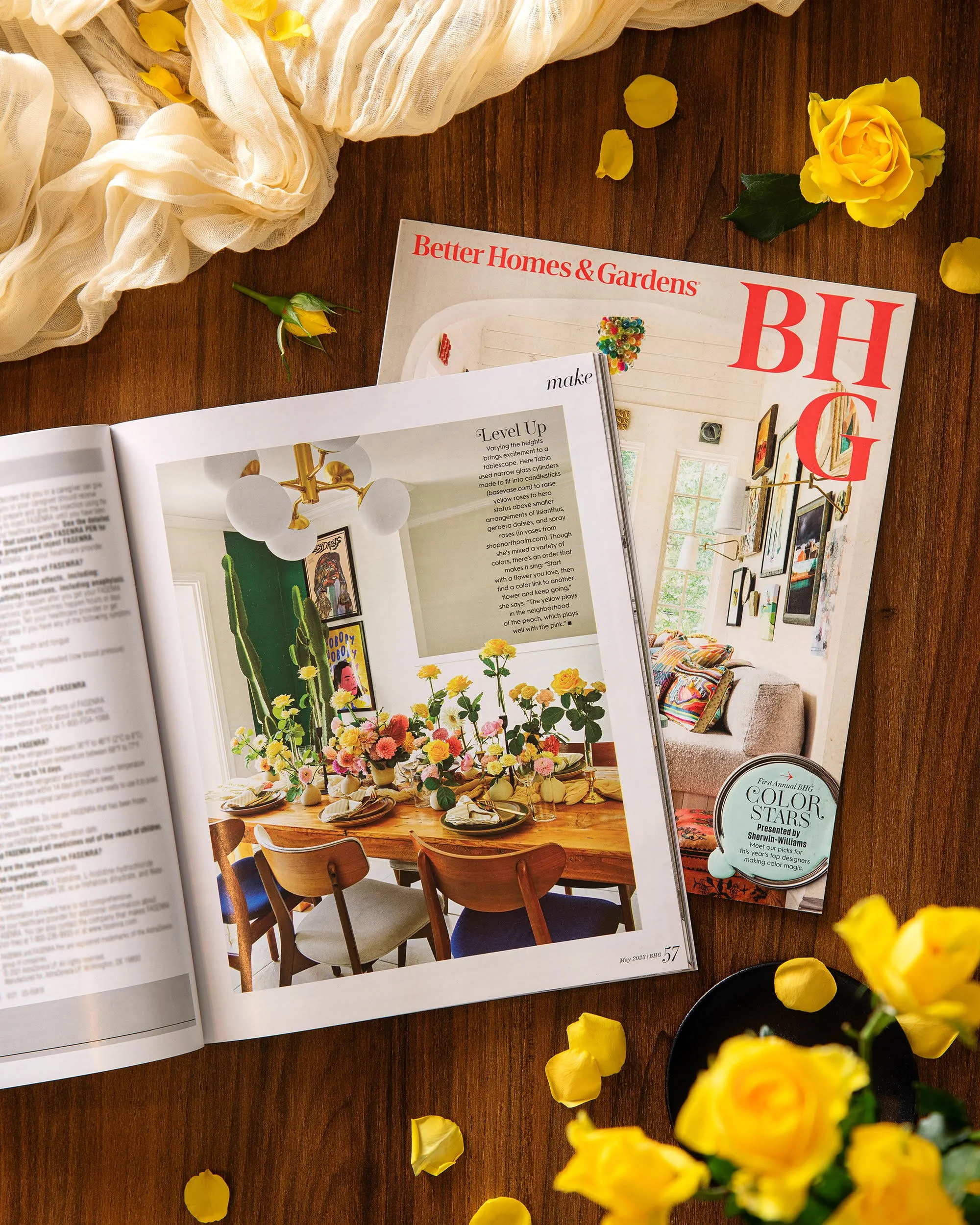 Open magazine on a wooden table with yellow flowers and a soft white fabric nearby