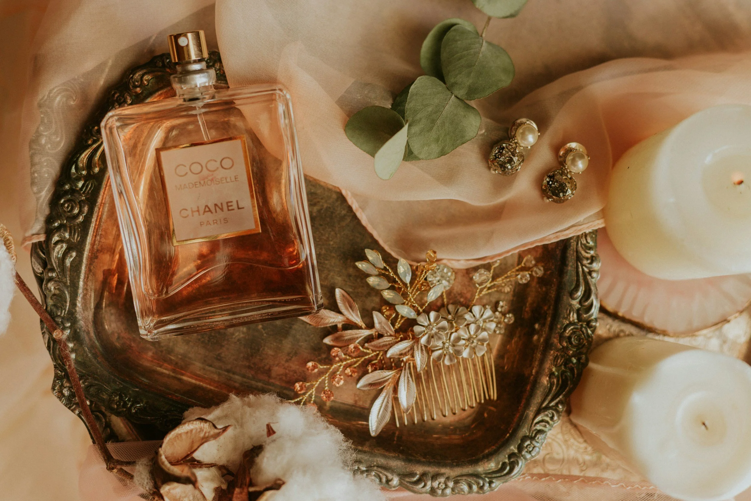 A flatlay of a luxury perfume bottle, cream candles, and golden accessories on a vintage tray, representing a gothic romance novelist visual brand identity
