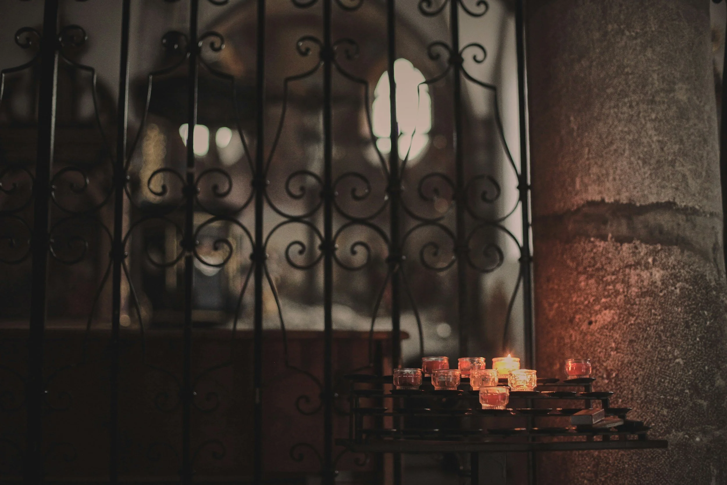 A cluster of white candles lit in front of a dark, historic stone window grate, demonstrating gothic author website design ideas