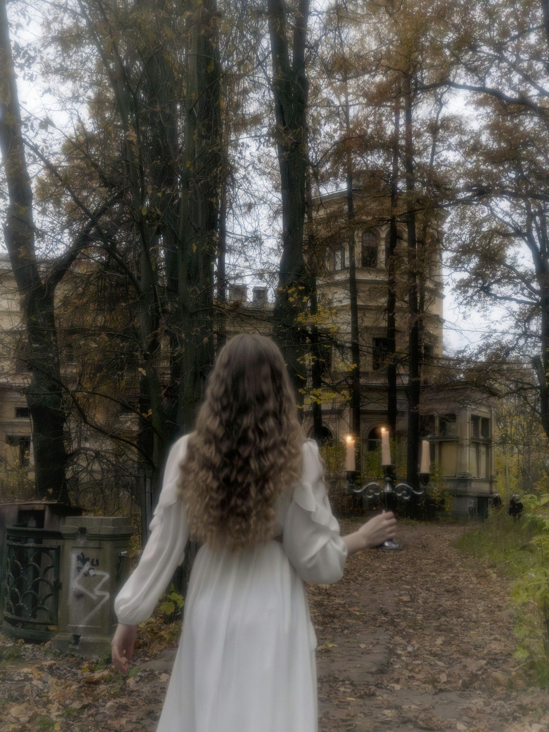 A back-view of a woman with long wavy hair looking toward a historic stone gothic estate in the woods, showing editorial photography styles for fiction writers